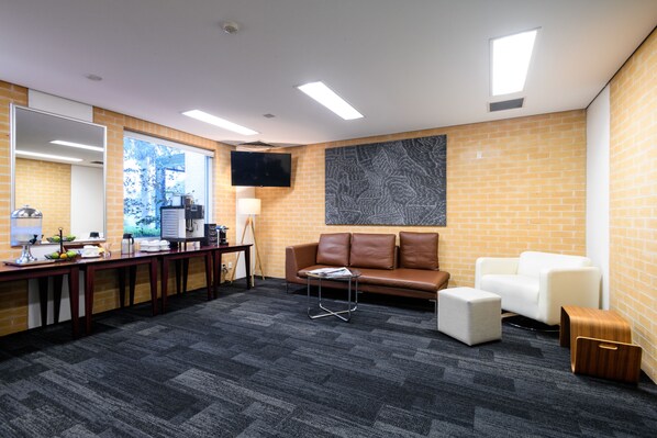 A modern office space with a brick wall, a leather couch, a white sofa, a small table, and a television mounted on the wall. - Lakeside Hotel and Conference Centre (Macquarie Park)