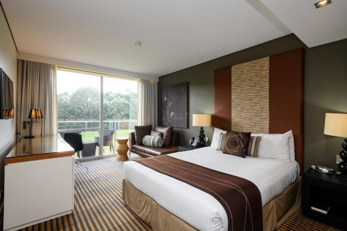 A hotel room with a large bed, a desk, a chair, and a view of the outdoors.