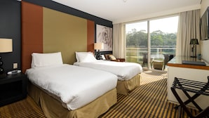 A hotel room with two beds, a desk, a chair, and a large window offering a view of the outdoors. - Lakeside Hotel and Conference Centre (Macquarie Park)