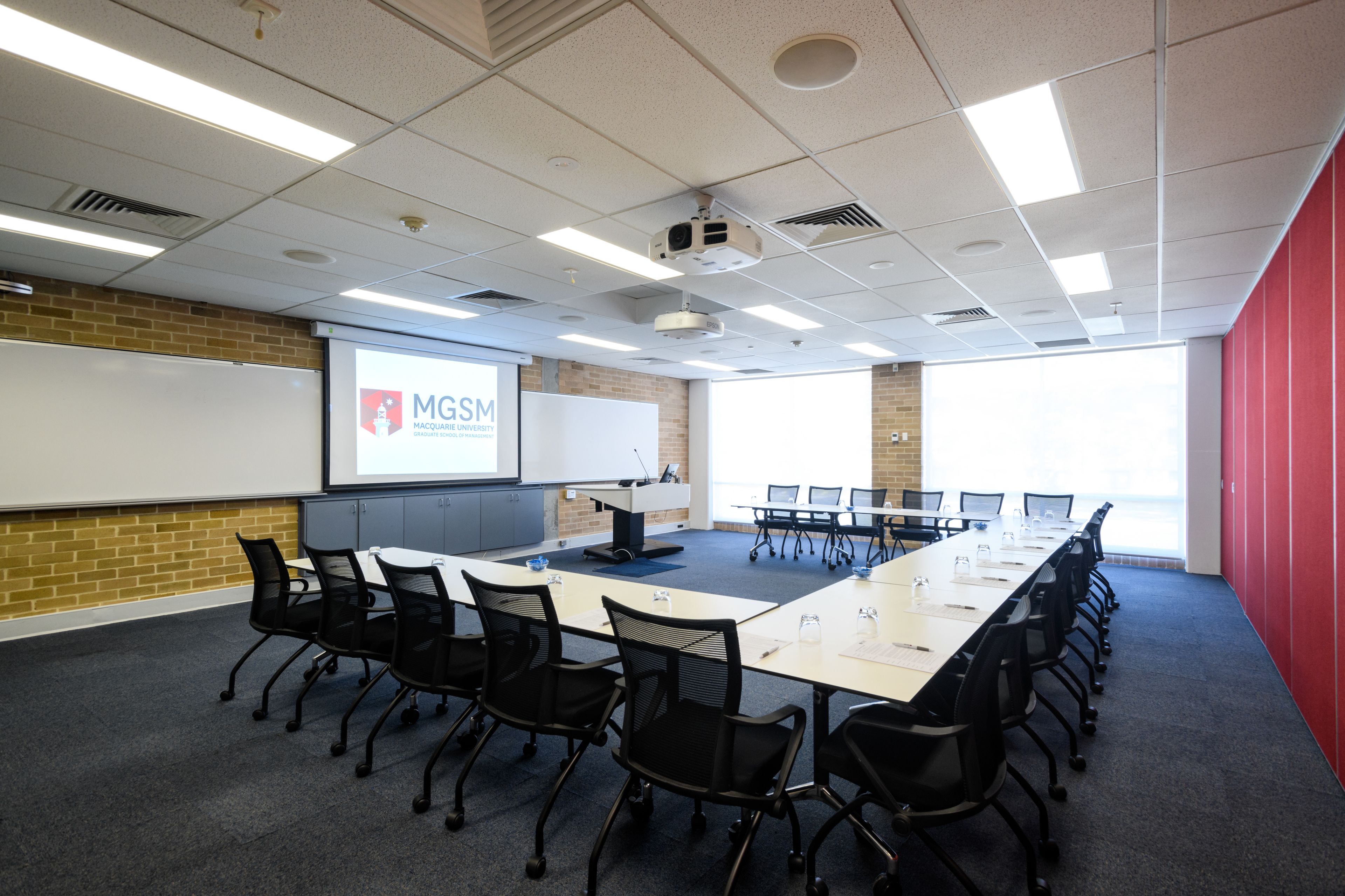 A conference room with a long table, black chairs, a projector screen, and a whiteboard.