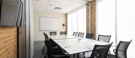 A conference room with a long table, black chairs, a whiteboard, and large windows.