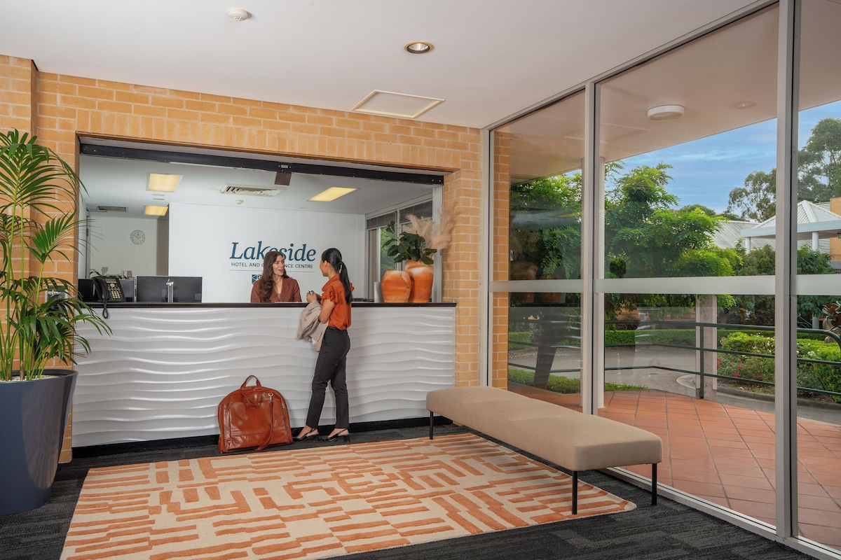 A reception area with a receptionist, a large potted plant, a bench, and a view of the outdoors.