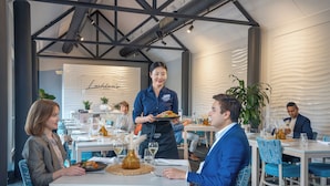 A restaurant with white tables, blue chairs, and a waiter serving food. - Lakeside Hotel and Conference Centre (Macquarie Park)