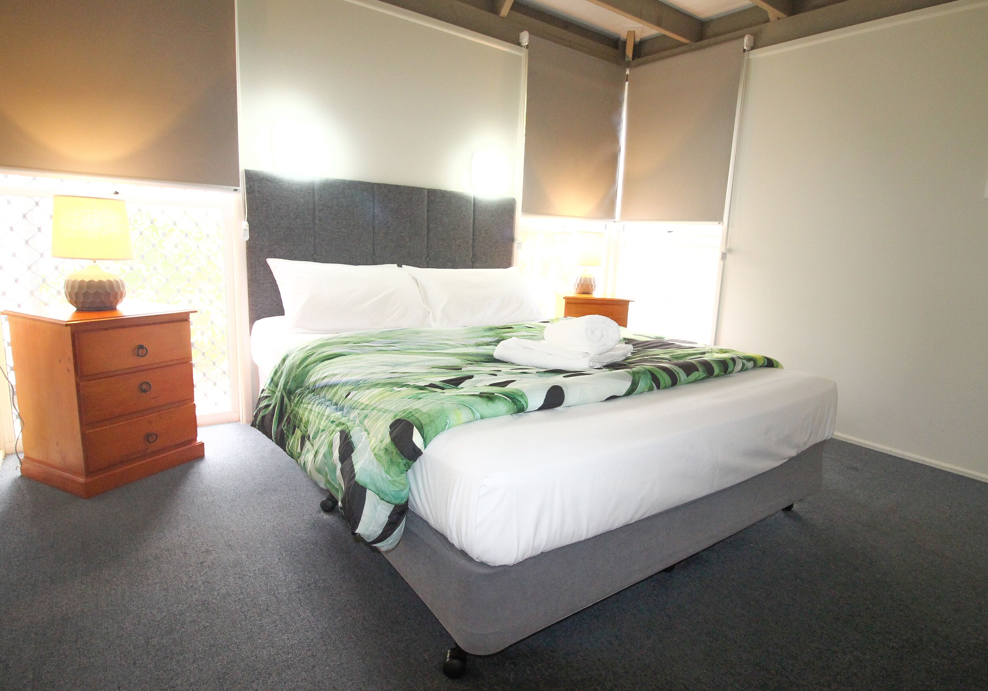 A bedroom with a bed, a nightstand, a dresser, and a window with blinds.