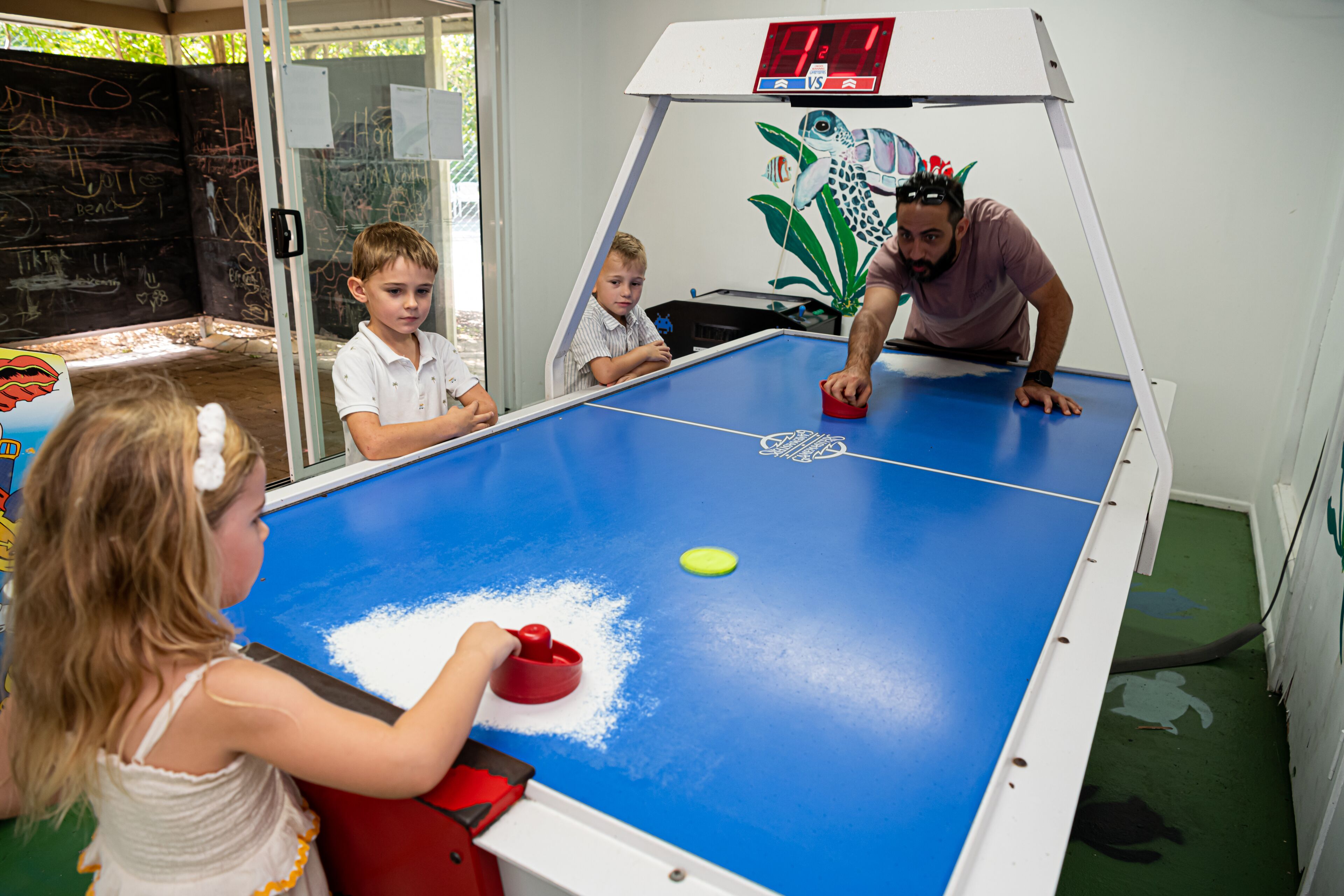 A table tennis table with a digital scoreboard, surrounded by children and an adult.
