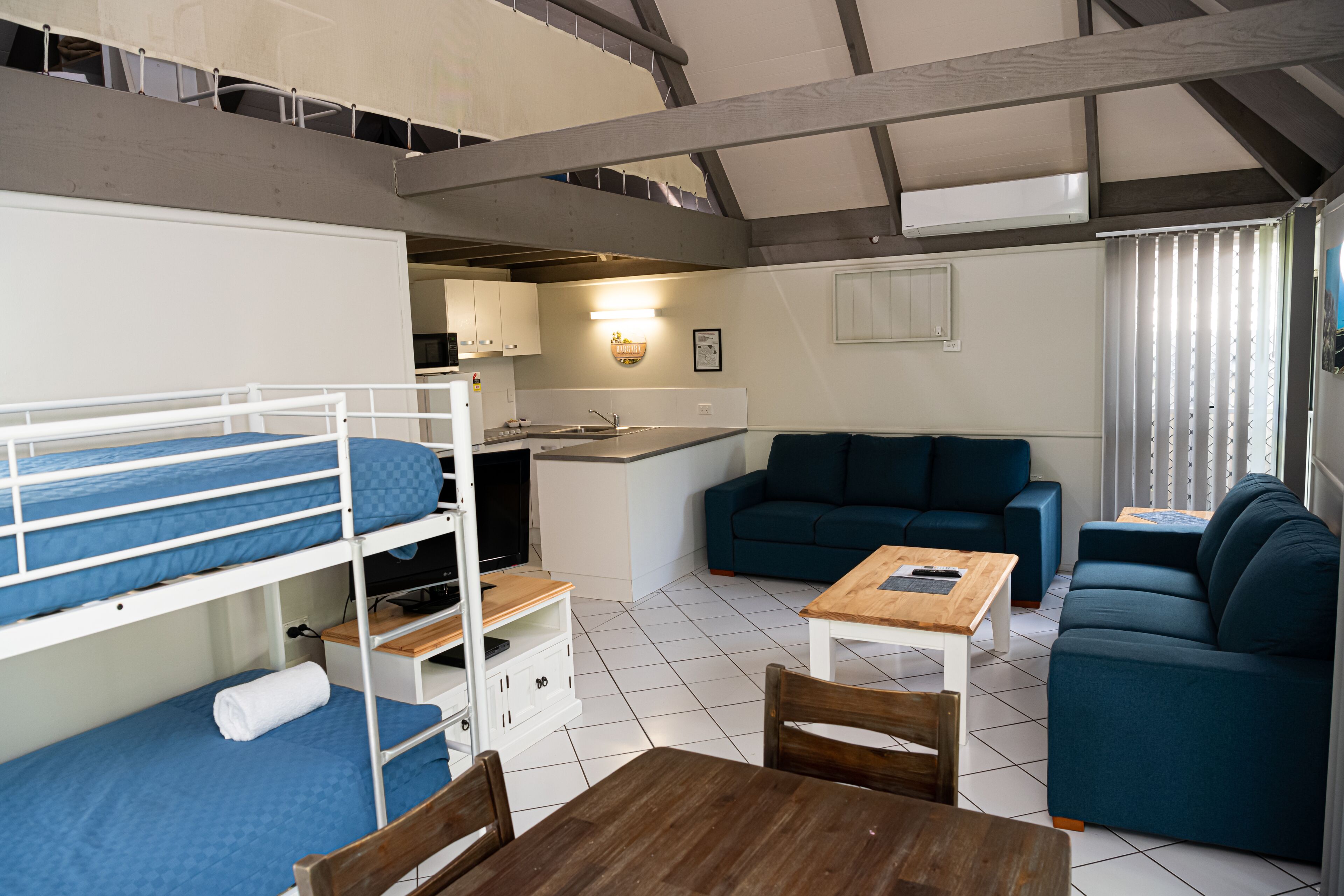 Una habitación funcional con literas, kitchenette, sofá y mesa de comedor.