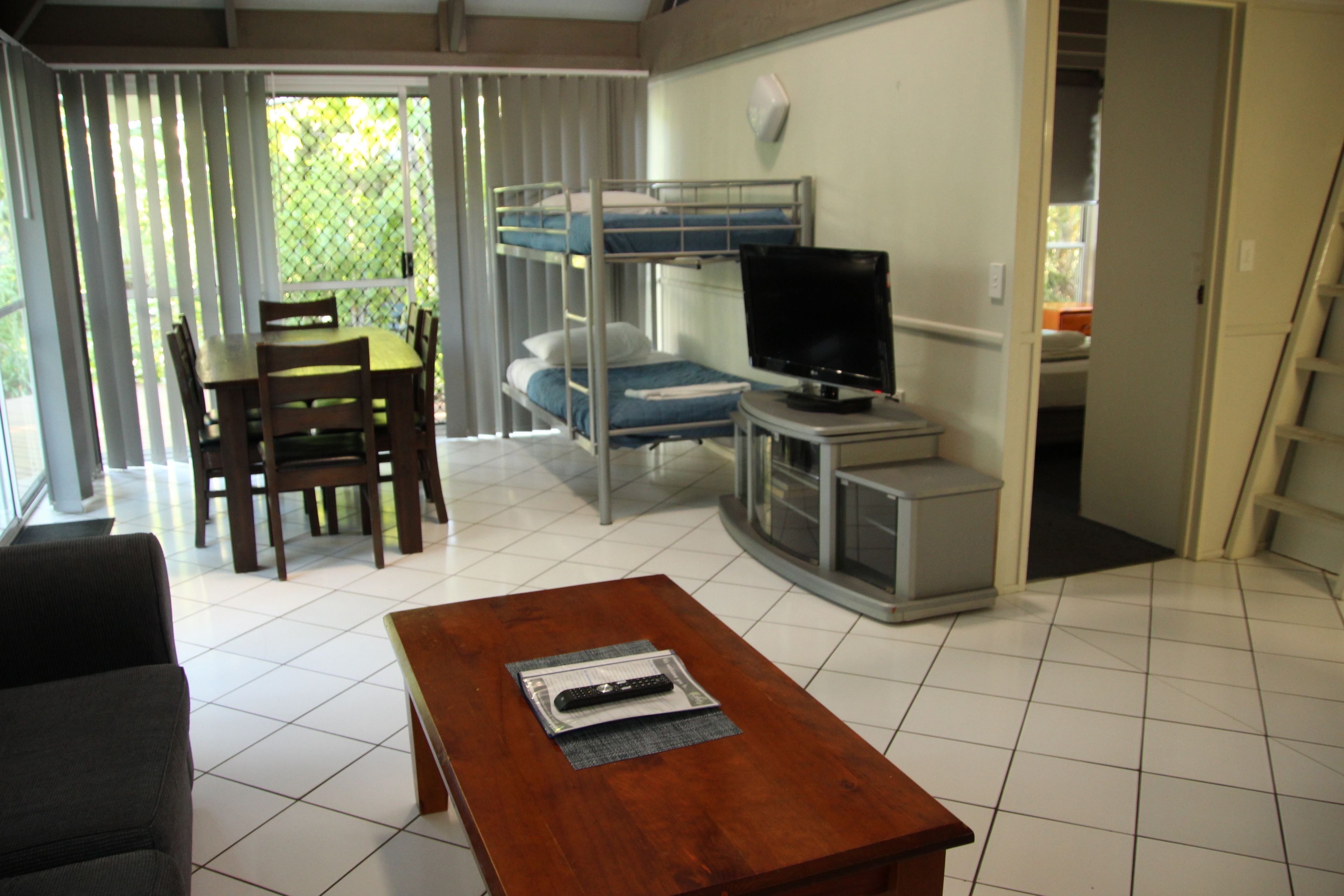 Un espacio habitable compacto con una cama litera, un televisor, una mesa de comedor con sillas y una mesa de centro.