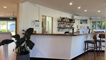 A bar area with a wooden counter, shelves with bottles, a laptop, and a potted plant.