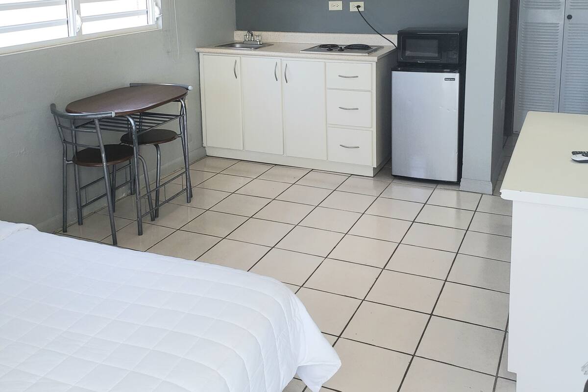 Une chambre compacte comprenant un lit, une petite kitchenette équipée d’un four à micro-ondes et d’un réfrigérateur, ainsi qu’une fenêtre avec des stores.