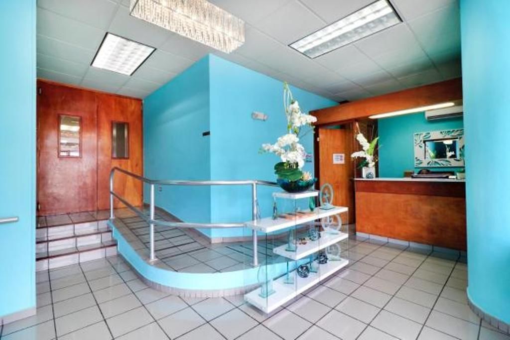 Una zona de recepción con pared azul, mostrador de madera, vitrina de vidrio y escalera con barandilla metálica.