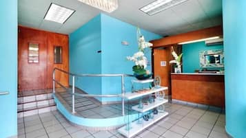 Una zona de recepción con pared azul, mostrador de madera, vitrina de vidrio y escalera con barandilla metálica.