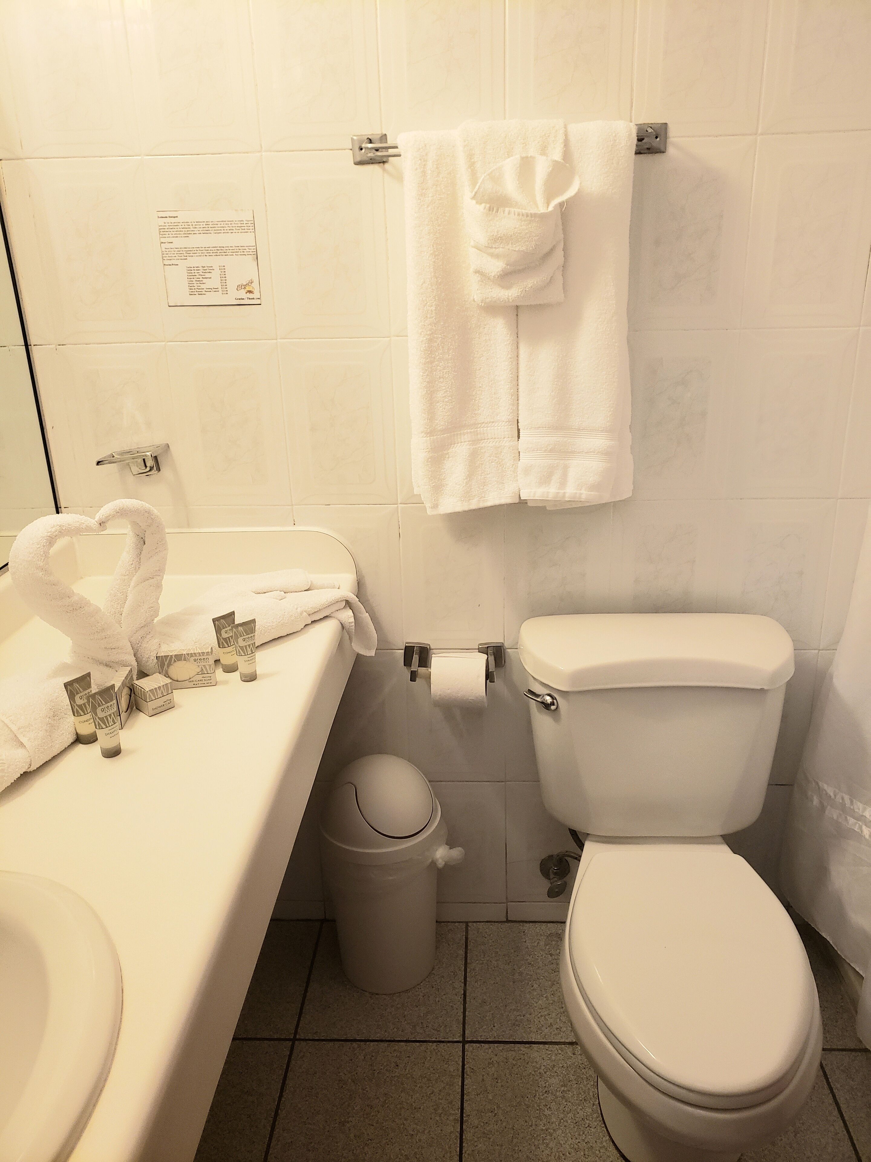 Une salle de bain comprenant des toilettes, un lavabo, une poubelle et un porte-serviettes avec une serviette pliée.