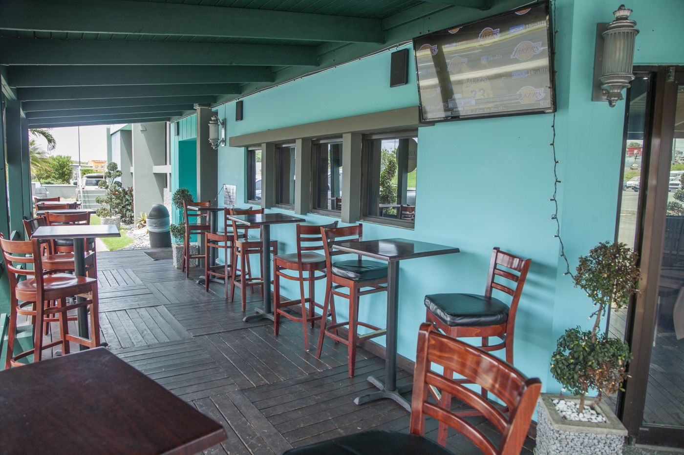 An outdoor patio with wooden tables and chairs, a covered area with teal walls, and a view of the street.