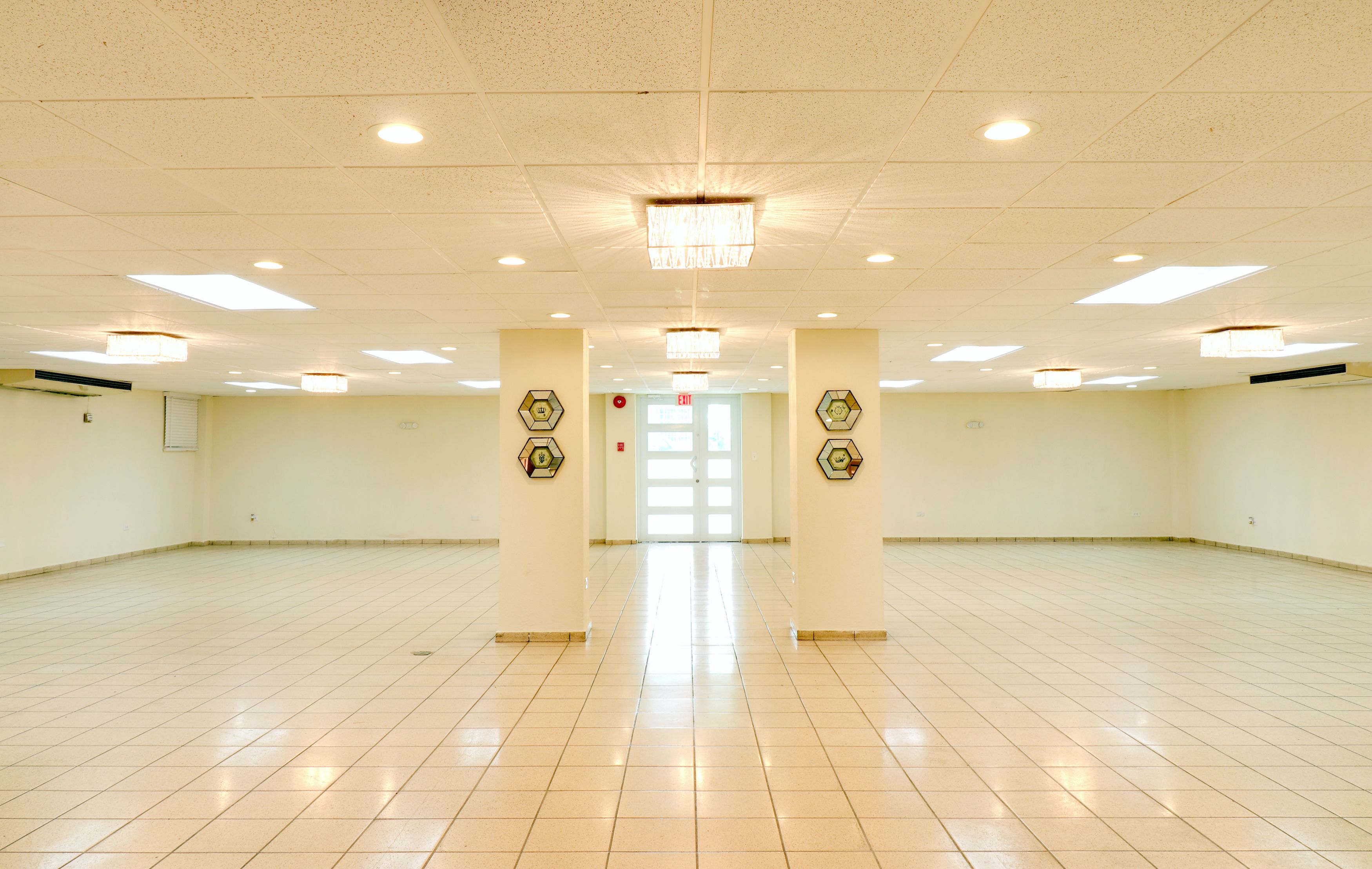 Une pièce spacieuse et bien éclairée, dotée d’un sol carrelé, de plusieurs luminaires au plafond et de panneaux muraux hexagonaux décoratifs.