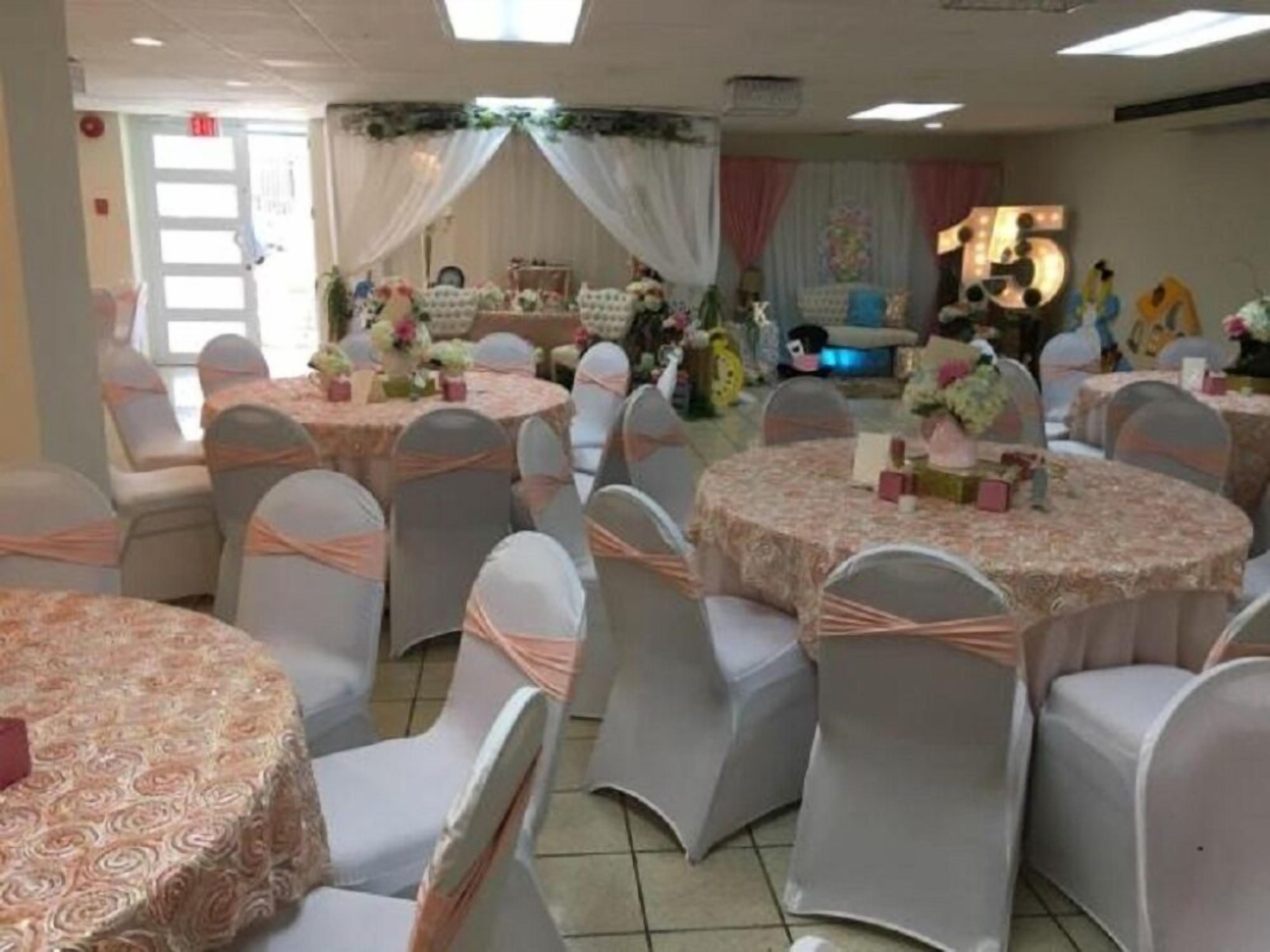 Une salle de banquet avec des tables rondes, des chaises et des centres de table floraux.