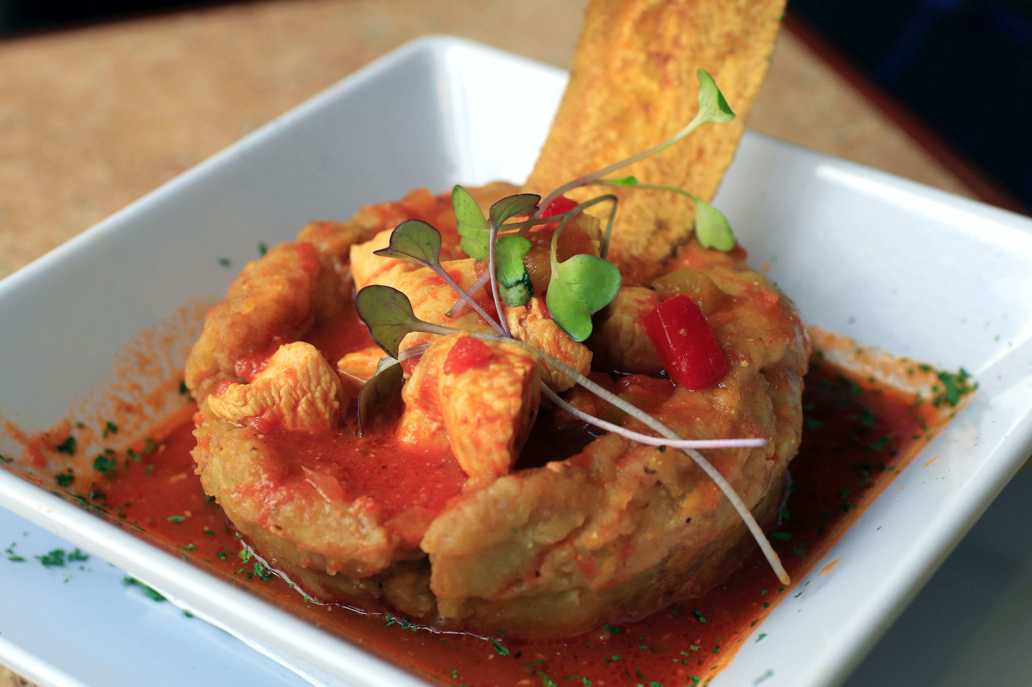 A dish with a crispy exterior, garnished with microgreens and a red sauce.