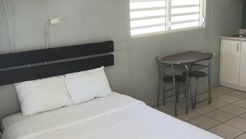 A hotel room with a bed, a small table with chairs, an air conditioning unit, and a window with blinds.