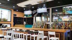 Zona de bar con sillas blancas y una barra de madera, con una variedad de botellas y una pantalla de televisión.