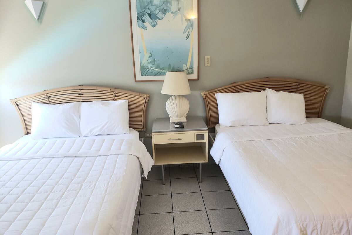 Une chambre d’hôtel avec deux lits, une table de chevet avec une lampe et un tableau au mur.