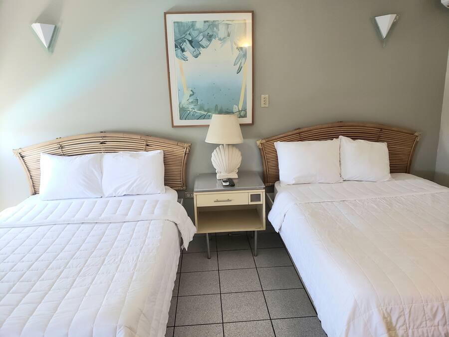 A hotel room with two beds, a nightstand with a lamp, and a painting on the wall.