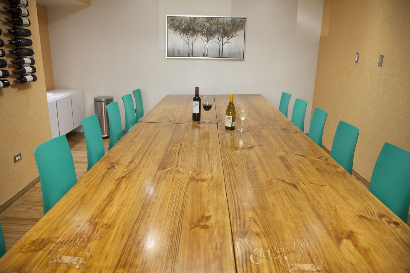 A conference room with a long wooden table, teal chairs, and a wine bottle on the table.