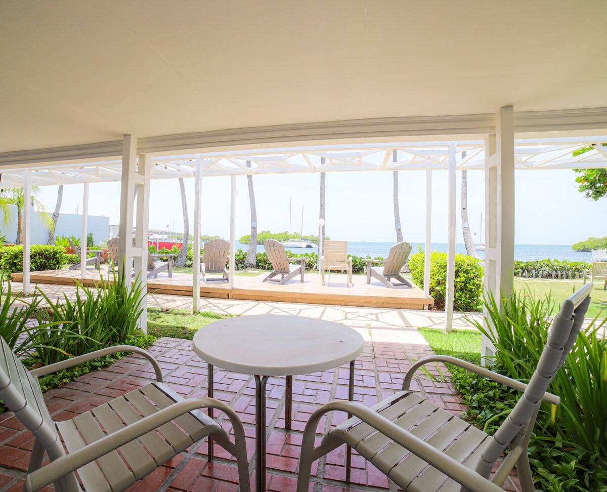 Un patio techado con una mesa y sillas, con vistas a una piscina y al océano.