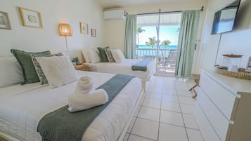 Habitació d'hotel amb dos llits, un balcó amb vista al mar i una televisió penjada a la paret.