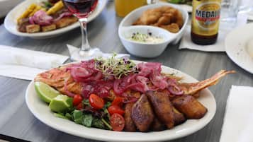 A dining table with a plate of food, a glass of red wine, and a bottle of beer.