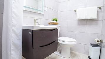 A modern bathroom with a toilet, a vanity with a mirror, and a trash bin.