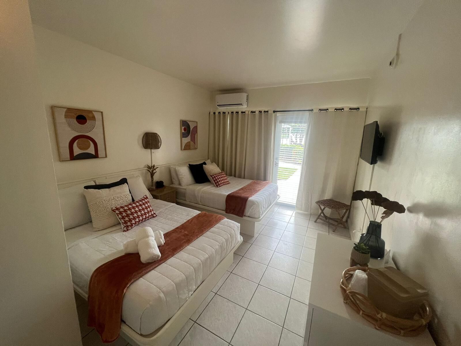 Habitación de hotel con dos camas, televisión, ventana con cortinas y una mesita con una planta.