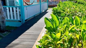 Un muelle de madera que conduce a una hilera de edificios coloridos, con un jardín tropical en primer plano.
