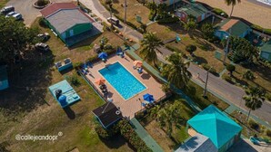 Vista aérea de un complejo turístico frente al mar, con piscina, acceso a la playa y vistas al océano.