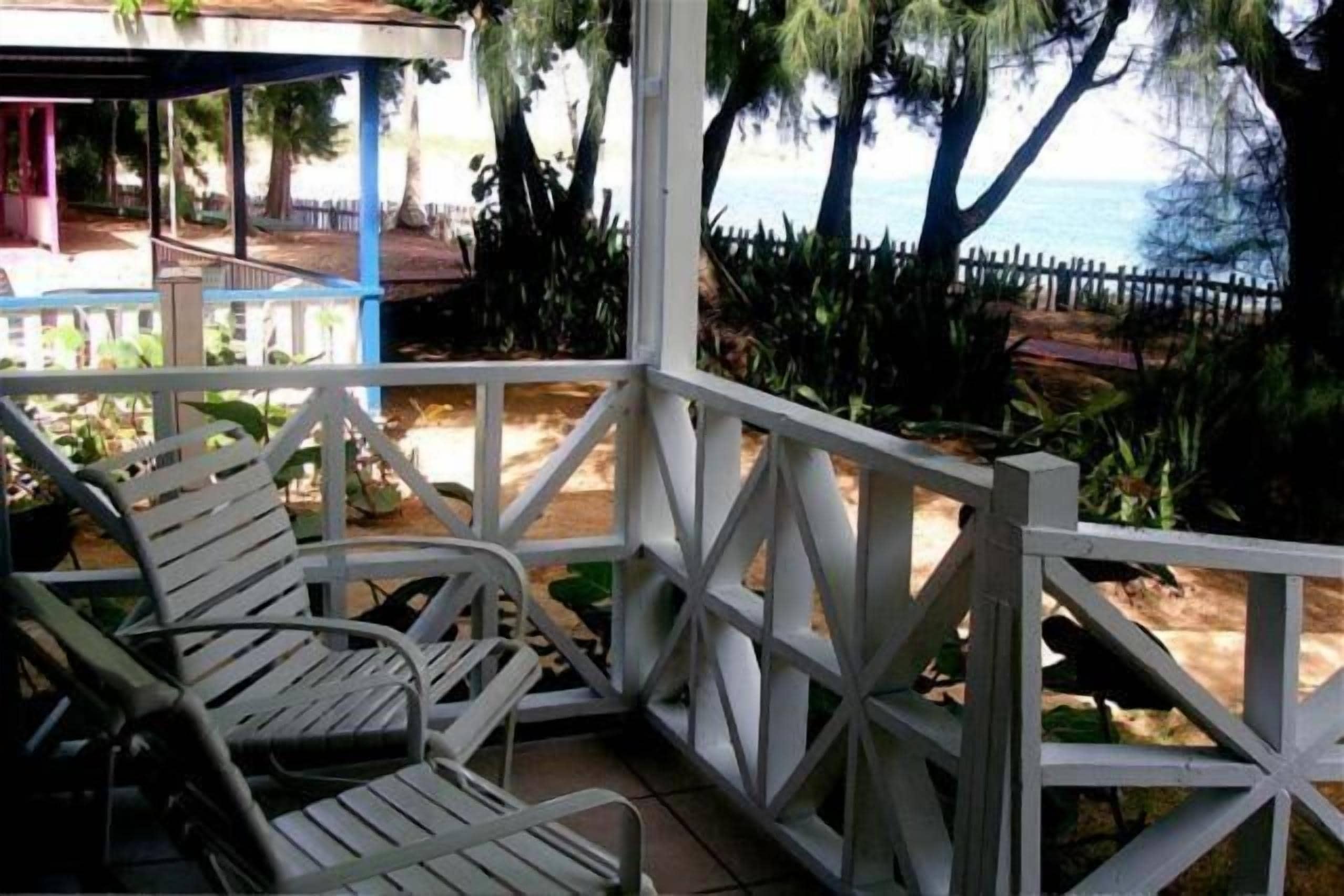 A covered outdoor seating area with white metal chairs and a white fence.