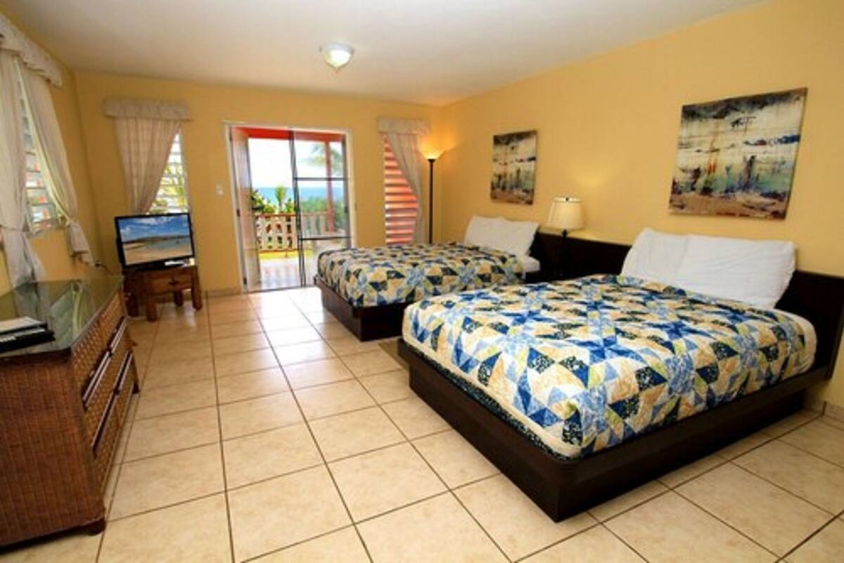 Quarto de hotel com duas camas, televisão, mesa de trabalho e varanda com vista.