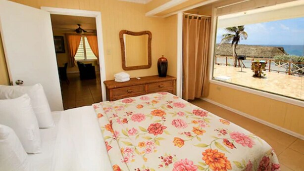 Habitación de hotel con cama, tocador, espejo y ventana con vista al mar.