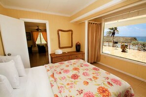 A hotel room with a bed, a dresser, a mirror, and a window with a beach view. - Parador Villas Del Mar Hau (Isabela)