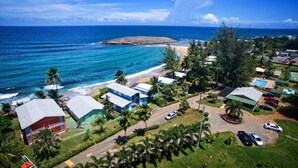 Un complejo turístico en la costa con acceso a la playa, varias edificaciones tipo cabaña y una vista despejada del océano.