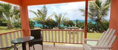 A balcony with a view of the ocean, a table, two chairs, and a railing.