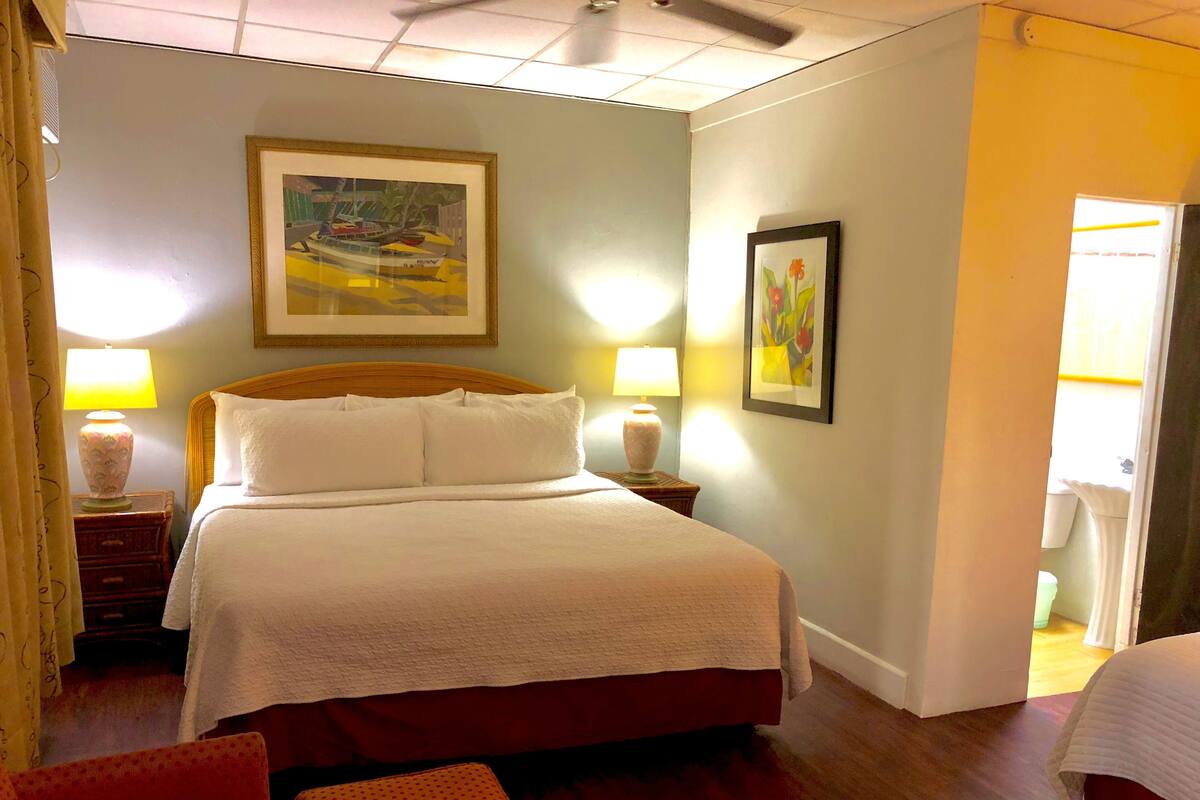 A hotel room with a bed, two bedside lamps, a painting on the wall, and a door leading to another room.