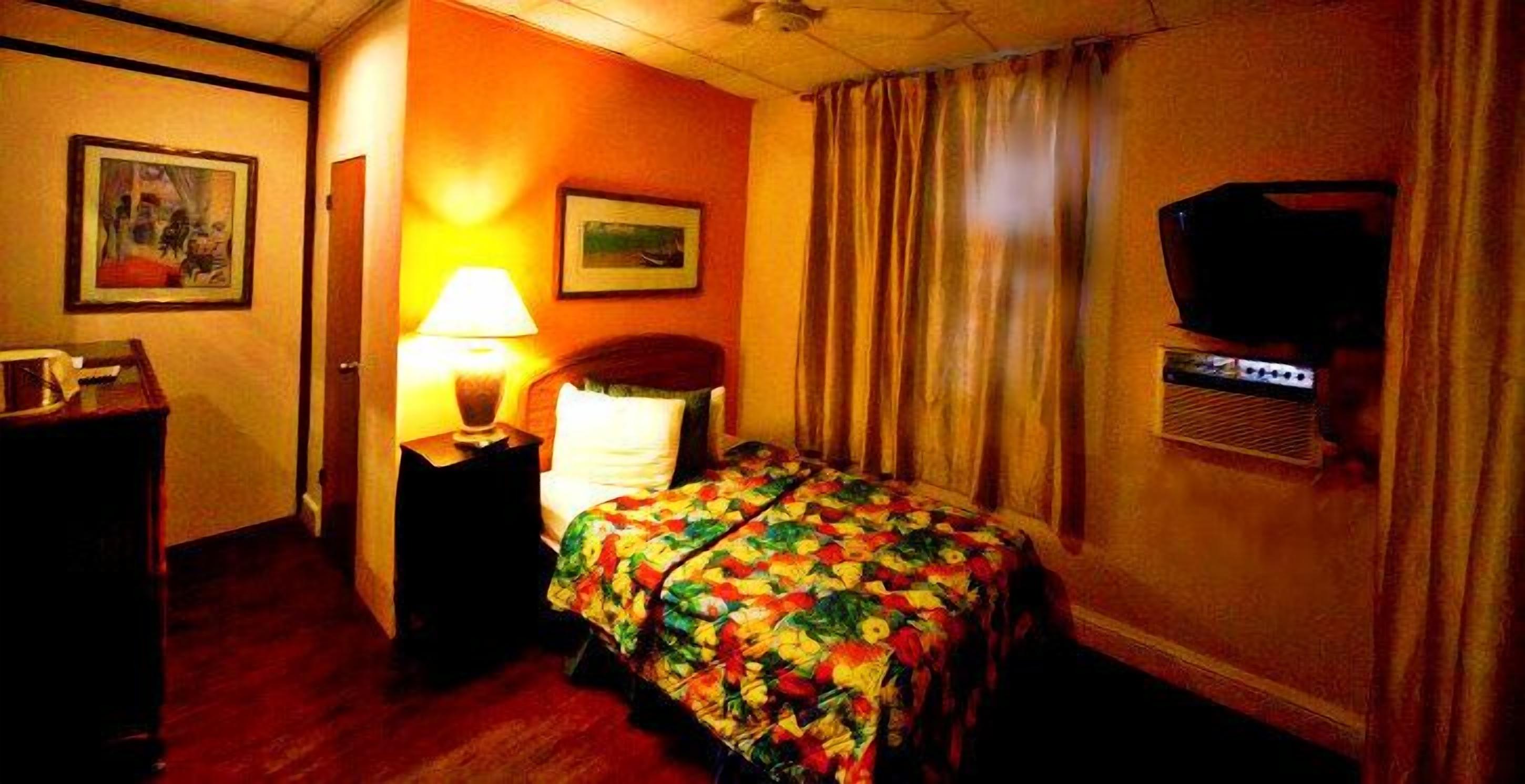 A hotel room with a bed, a nightstand, a lamp, a television, and a painting on the wall.