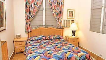 Un dormitorio con cama, mesita de noche, lámpara, ventilador de techo y ventana con cortinas.