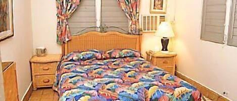 A bedroom with a bed, a nightstand, a lamp, a ceiling fan, and a window with curtains.