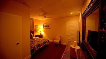 Ein Hotelzimmer mit einem Bett, einem Sessel, einem Schreibtisch mit Lampe, einem Spiegel und einer Tür.