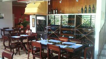 An indoor dining area with wooden tables and chairs, a wine rack with bottles, and a tiled floor.