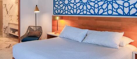 A hotel room with a large bed, a nightstand, a wall-mounted lamp, and a decorative geometric wall panel.