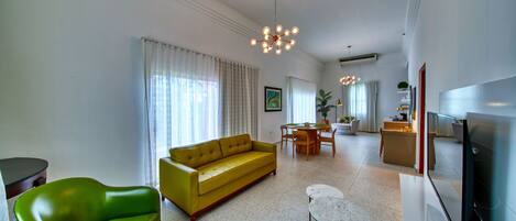 A modern living room with a yellow sofa, a green armchair, and a dining area with a table and chairs.