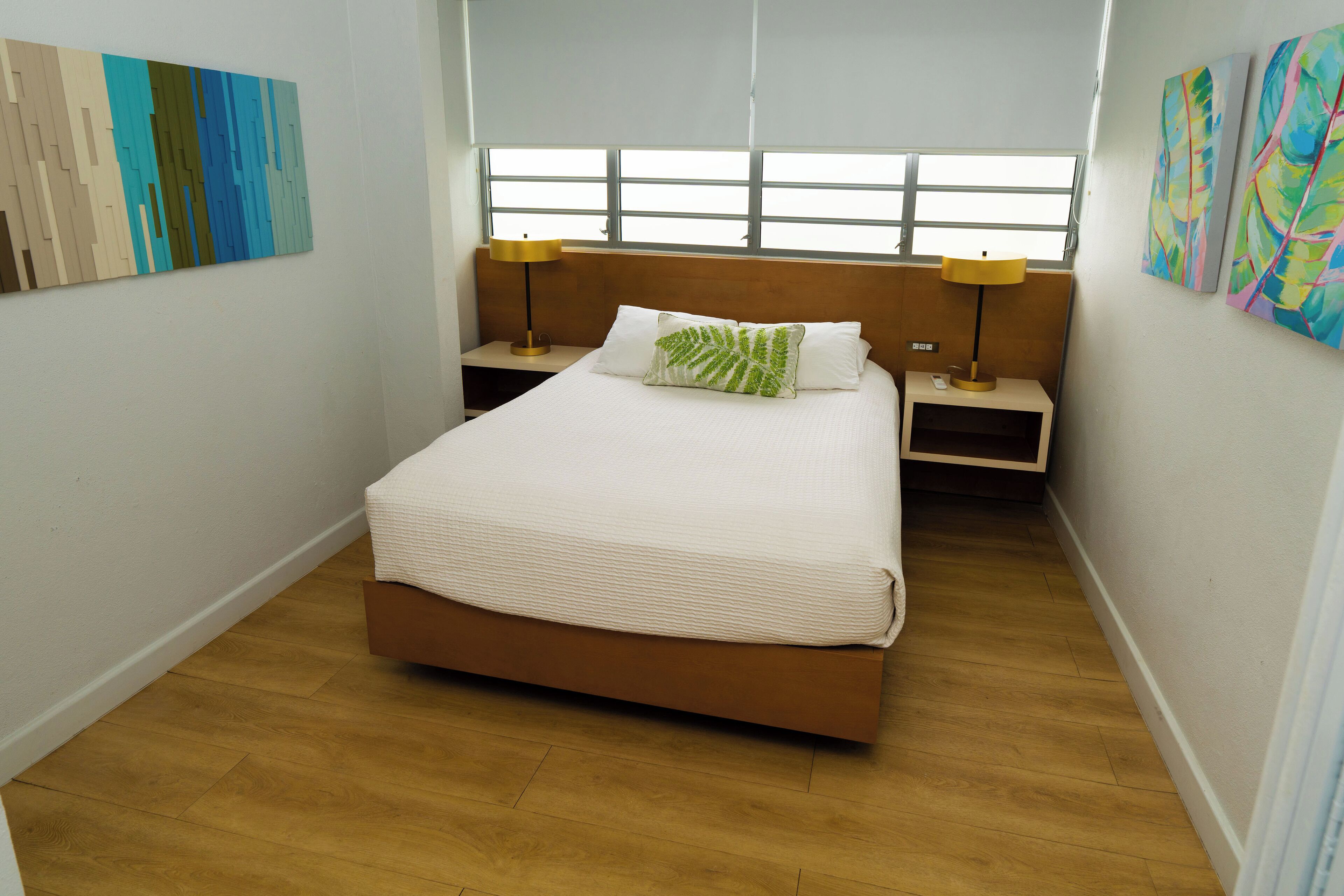 Ein Schlafzimmer mit einem Bett, zwei Nachttischen, einem Fenster und Bildern an den Wänden.