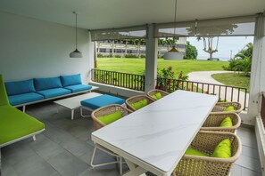 A covered outdoor area with a white table and chairs, a blue sofa, and wicker chairs with green cushions. - Rincon of the Seas - Grand Caribbean Hotel (Rincon)