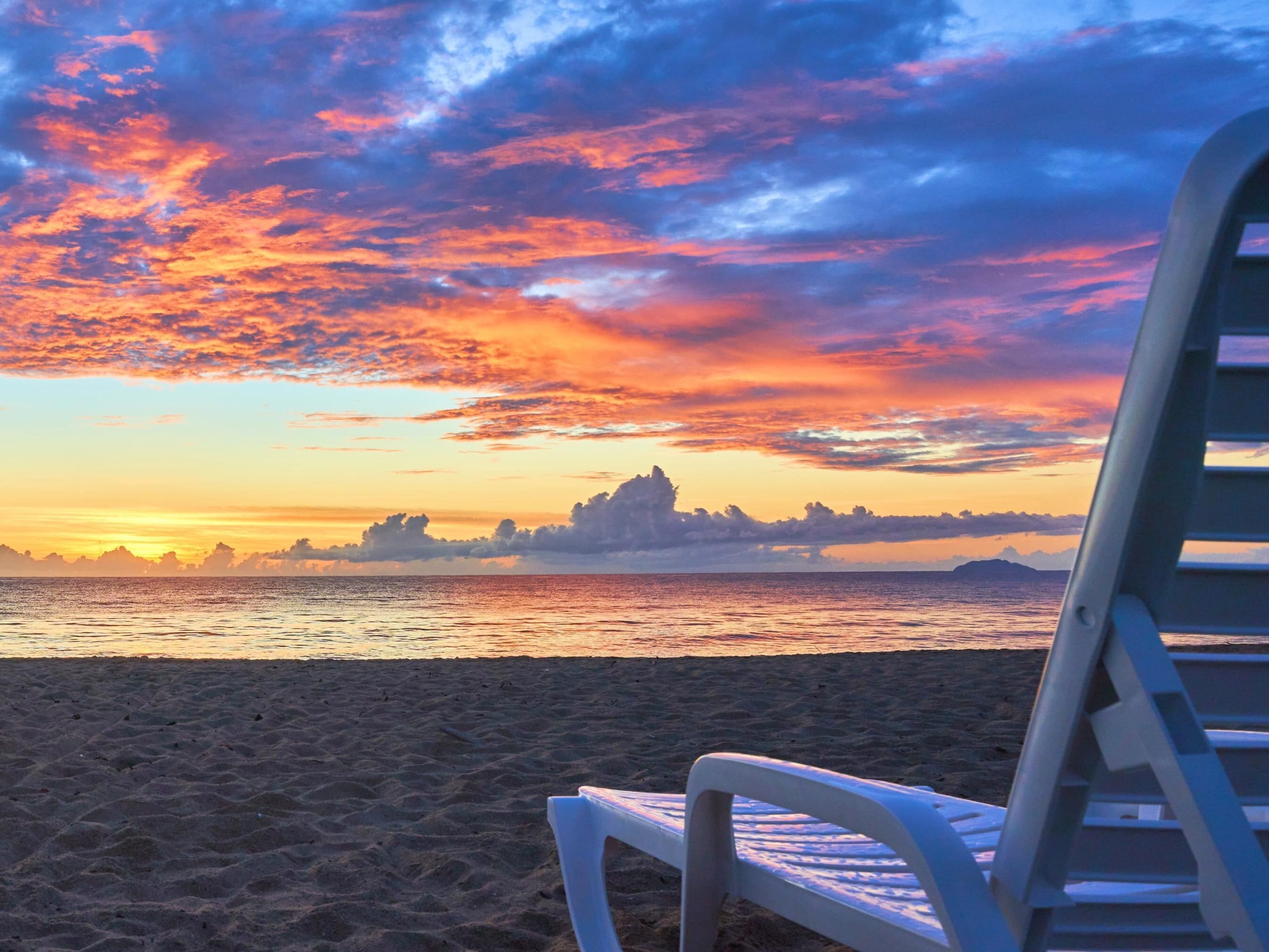 A beach with a sunset, a chair, and distant landforms.