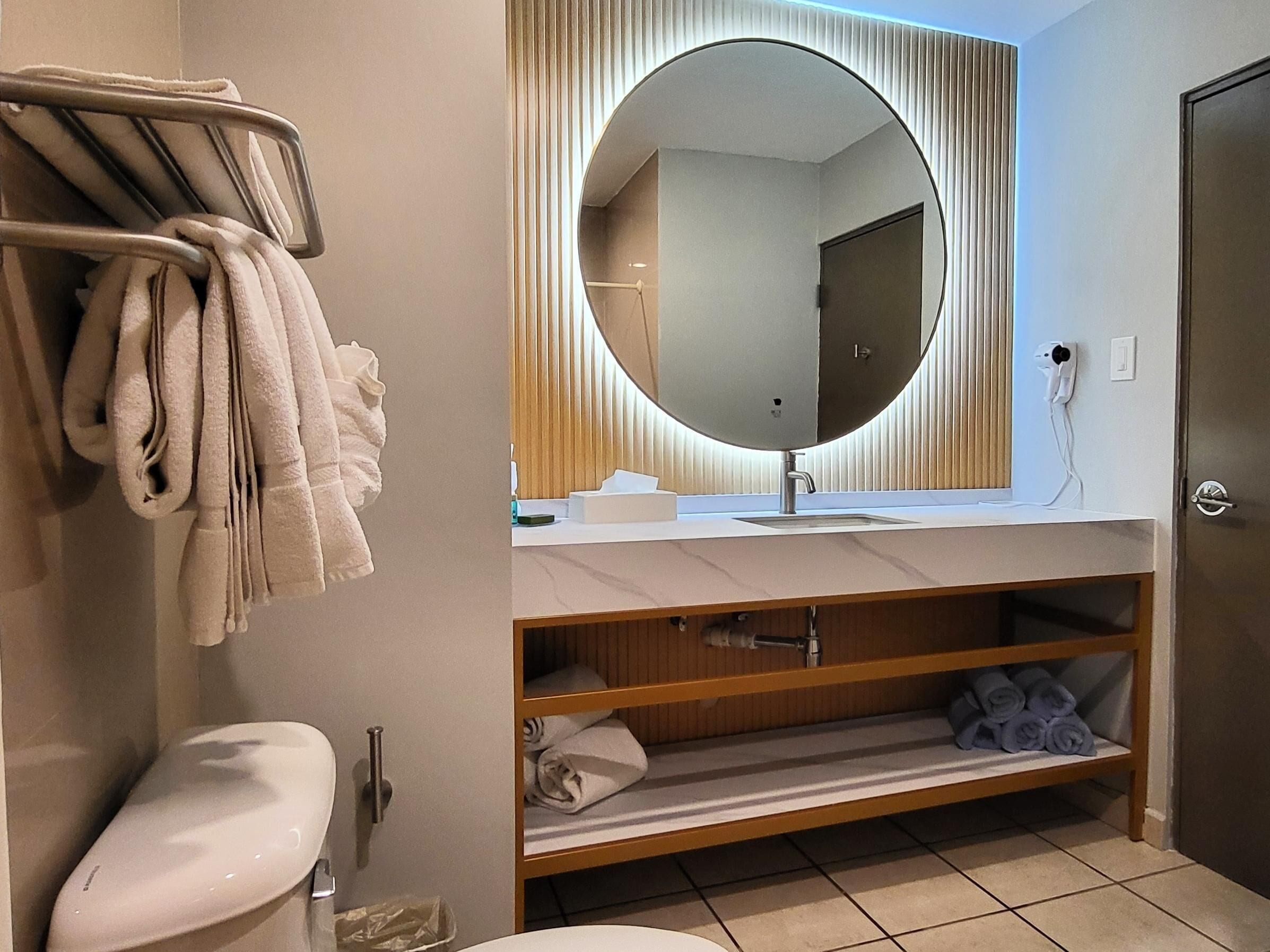 A modern bathroom with a round mirror, a toilet, and a towel rack.
